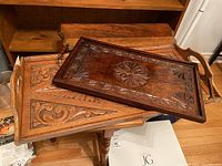 Two wood serving trays stacked showing carved details and handles, highlighting difference in wood tone and pattern