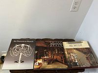 Three Art Nouveau coffee table books laid out next to each other showing front covers with metalwork sculpture, interior dining furniture, and architectural design