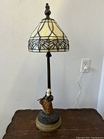 Full view of the table lamp showing the stained glass shade, dancing lady figure, and base with cord plugged into outlet.