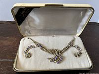 Complete boxed set including necklace and pair of clip-on earrings on velvet display inside a satin-lined box.