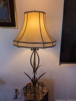 Full view of the vintage bronzed metal plant form table lamp turned on, showing the beige fabric shade and metal base with leaf motifs.