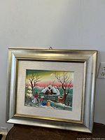 Front view of Croatian naive winterscape oil painting in silver frame hung on wall.