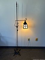 Full view of the Gothic cast-iron tri-footed floor lamp standing 62 inches tall with lantern illuminated, plugged into power.