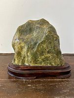 Front view of nephrite jade mountain sculpture on carved rosewood base showing natural color and texture.