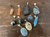 Photo of all 10 pendants laid out on wooden surface showing variety of shapes, colors, and types of semi-precious stones.