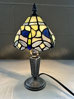 Front angle view of petite stained glass table lamp showing bluebell floral shade and metal base with floral motifs.