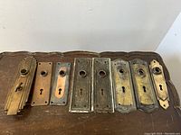 Full set of eight brass and copper door key cover plates displayed on wooden surface.