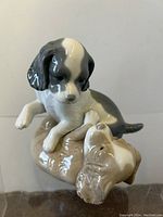 Front view of porcelain figurine showing the black and white puppy with a raised paw over the smaller light brown and white puppy.