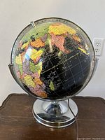 Globe front view showing world map on black background with chrome meridian and base