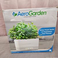 Front view of AeroGarden Harvest box showing image of the garden system with green leafy herbs inside, AeroGarden logo and branding.