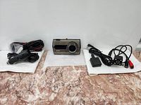 Full view of all parts of the dash cam set laid out on a floor with main camera, charger cable, power adapter, and rear camera.