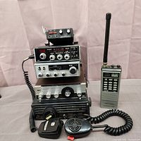 Front view of five CB radios: four stacked base/mobile units and one handheld transceiver with numeric keypad and antenna.