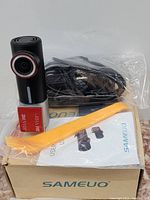 Photo shows black Sameuo dash camera, USB cable in plastic wrap, yellow plastic tool, user manual, and the original box with brand name.