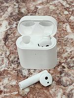 White wireless Bluetooth earbuds with one earbud inside an open white charging case, on a marble textured surface, showing the condition and design.