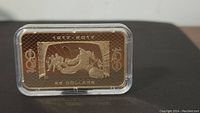 Front side of gold plated bullion bar showing a sports or historic scene, date range 1917-2017, and denomination of 5 dollars