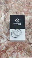 Jakcom branded box with silver smart ring on top, showing product from above on a pink marble surface
