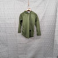 Single green men's hoodie sweatshirt on hanger against grey backdrop. Visible hole on front lower part of the hoodie.