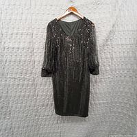 Black sequin dress hanging on wooden hanger against a white textured background.