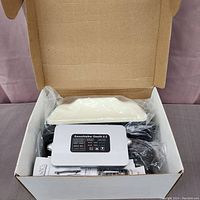 Open cardboard box showing Smooth Talker Stealth X-2 device, cables, white antenna and instructions inside plastic wrapping.