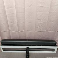 Front view of black BOMAKER ODINE 1 soundbar with accompanying remote control placed in front.