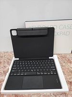 Black tablet keyboard case with Bluetooth keyboard, clip for tablet, and rear camera cutout shown inside packaging box.