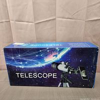 Photo of the telescope packaging box showing the telescope with tripod and smartphone mount against a starry background graphic.