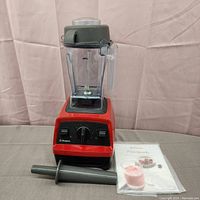 Red Vitamix Explorian E320 blender with container, lid, tamper and manual on grey surface