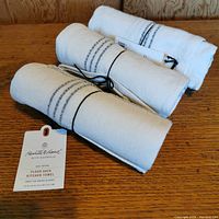 Three rolled white flour sack kitchen towels tied with black string on a wooden surface, showing overall lot contents.