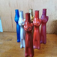 Set of six colorful cat-shaped glass wine bottles arranged in two rows on wood surface