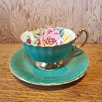 Front view of the Aynsley Green Cabbage Roses teacup and saucer showing floral rose interior, green exterior, and gilded trim.
