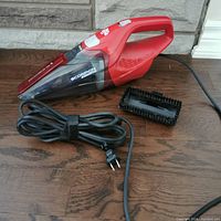 Red Dirt Devil Scorpion Quick Flip corded hand vacuum with power cord wrapped and separate brush accessory on wooden surface.