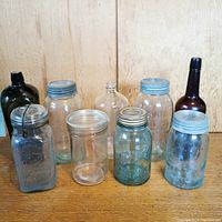 Front view of nine vintage glass bottles and jars with various lids and colors