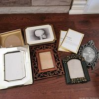 All 8 assorted picture frames arranged on wood floor showing variety of sizes and styles including two sealed gold-tone plastic frames.