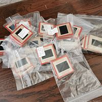 Multiple plastic bags containing stacks of red-bordered photographic slides laid out on a wooden table.