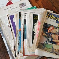 Stack of vintage magazines and advertisements with diverse colorful covers and visible wear