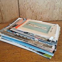 Stack of vintage needlework and stitching pamphlets, showing worn edges and a variety of sizes.