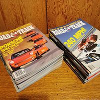 Two stacks of Road & Track magazines displaying cover images highlighting Porsche cars and racing cars with bold yellow and white text.