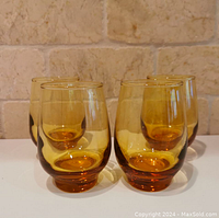 Four amber vintage drinking glasses grouped together on a white surface with stone textured background. Shows color and set quantity.