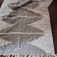 Full view of the folded grey and white jute rug showing geometric patterns and tassels.