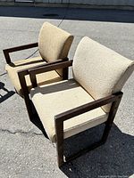 Front and side view of two mid-century modern armchairs showing beige fabric upholstery and dark wood rectangular armrests and legs