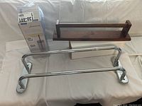 Photo of bathroom accessories including a boxed AmazonBasics toilet brush, wooden towel rack, and two chrome towel bars.