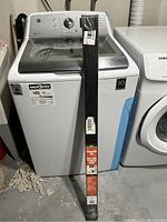 Full view of brand new MD garage door bottom seal in packaging, standing against a washing machine.