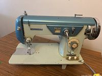 Front and side view of vintage Kenmore Deluxe sewing machine with stitching mechanisms and controls visible, showing metal casing and color scheme.
