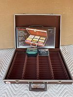 Open brown cassette storage case with multiple slots. Brand new boxed case sitting inside for comparison.