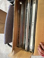 Box containing multiple metal drawer slide rails stacked upright in a cardboard box. The rails are metallic silver with mounting holes and ball bearing tracks.