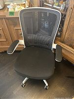Front view of the ergonomic office chair showing black mesh back, black fabric seat, white frame, and armrests