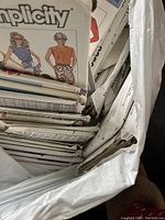 Large collection of folded paper sewing pattern envelopes in plastic bag including patterns from Simplicity brand.