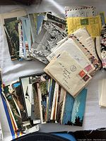 Photo shows multiple vintage postcards, airmail envelopes, and some handwritten letters laid out on a white surface.