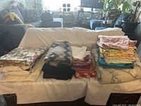 Photo showing three piles of folded fabric pieces on a white-covered table or sofa with floral, geometric, solid, and leaf patterns visible.