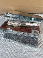 View of the stack of seven individually wrapped bedding sheets with assorted patterns, placed against a cardboard background on a quilted surface.